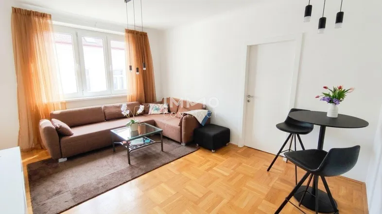 Gemütliches Wohnzimmer mit braunem Ecksofa, Parkettboden und Blick nach draußen.