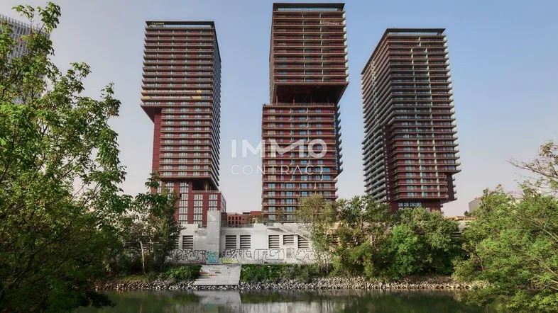 Moderne Hochhäuser mit markanter Architektur am Wasser, umgeben von Bäumen und Grünflächen.