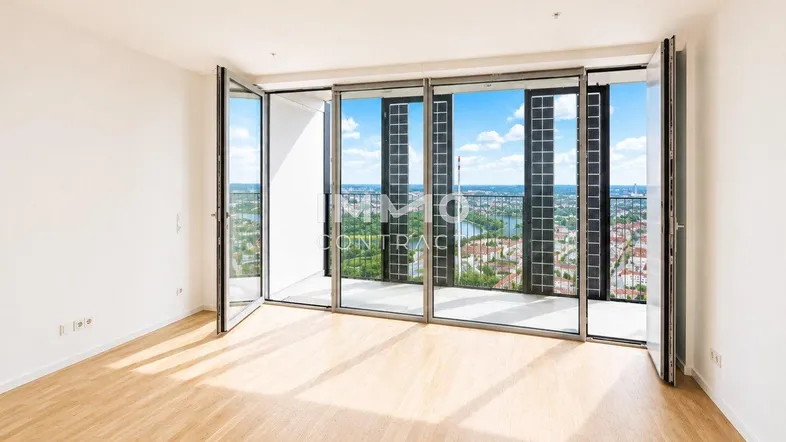 Helles, leeres Zimmer mit Holzboden und raumhohen Fenstern, die einen weiten Stadtblick bieten.