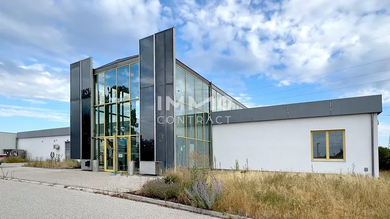 Moderne Gewerbeimmobilie mit großer Glasfassade und umliegender Grünfläche unter bewölktem Himmel.
