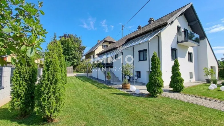 Weißes Einfamilienhaus mit gepflegtem Rasen und modernem Anbau unter blauem Himmel.