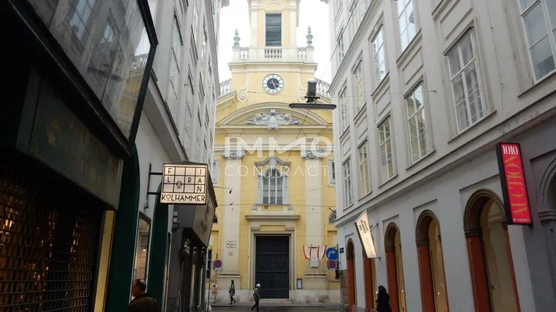 Blick auf eine belebte Straße mit Geschäften und einer historischen Kirche im Hintergrund.