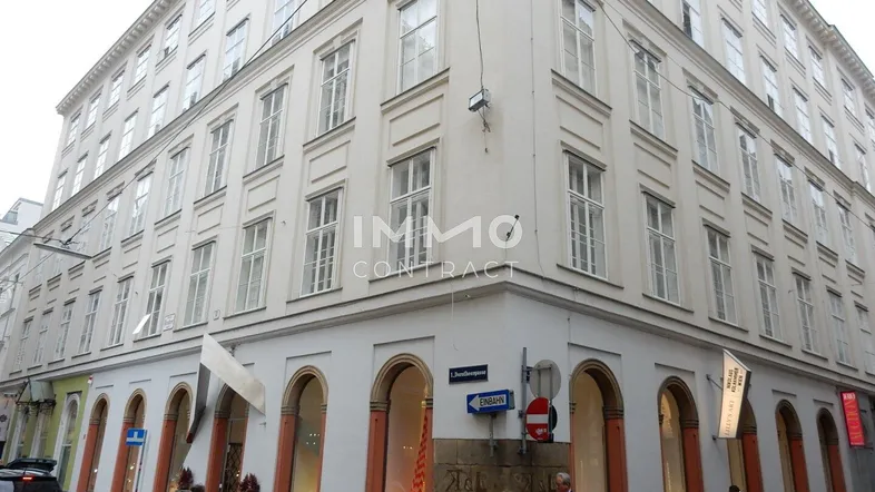 Historisches Eckgebäude mit vielen Fenstern und Geschäften im Erdgeschoss in einer belebten Straße.