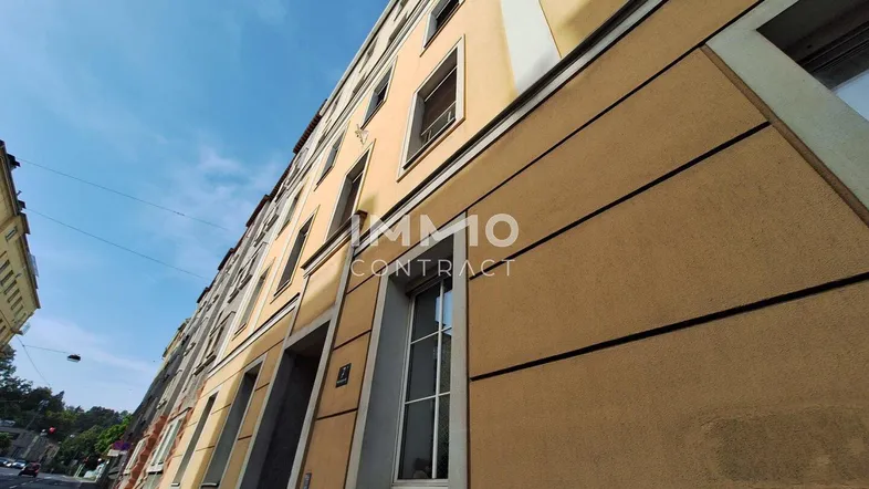 Fassade eines Mehrfamilienhauses mit gelb-beiger Farbgebung unter blauem Himmel.