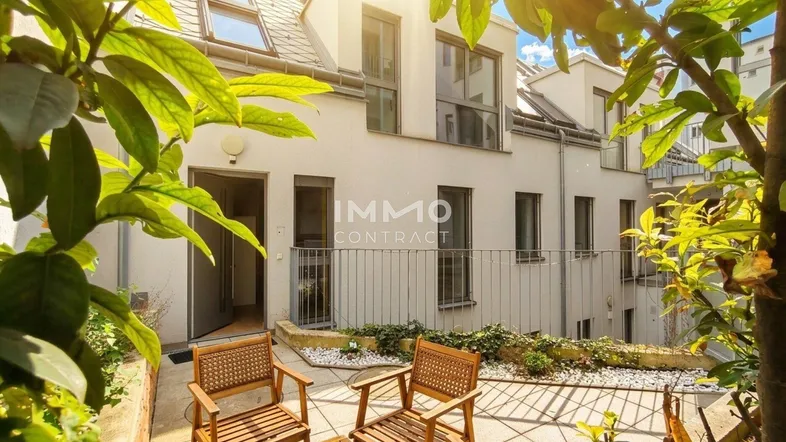 Sonnige Terrasse mit Sitzgelegenheiten und Blick auf die moderne Gebäudefassade.