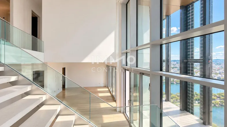 Helles Treppenhaus mit moderner Glasbrüstung, hohen Decken und weitem Blick auf die Stadt und den See.