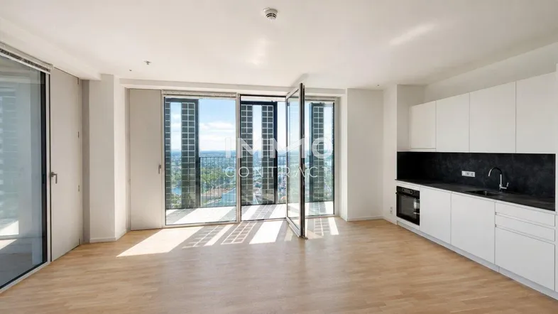 Helles, offenes Wohnzimmer mit integrierter Küche, Parkettboden und Zugang zu einem Balkon mit Stadtblick.
