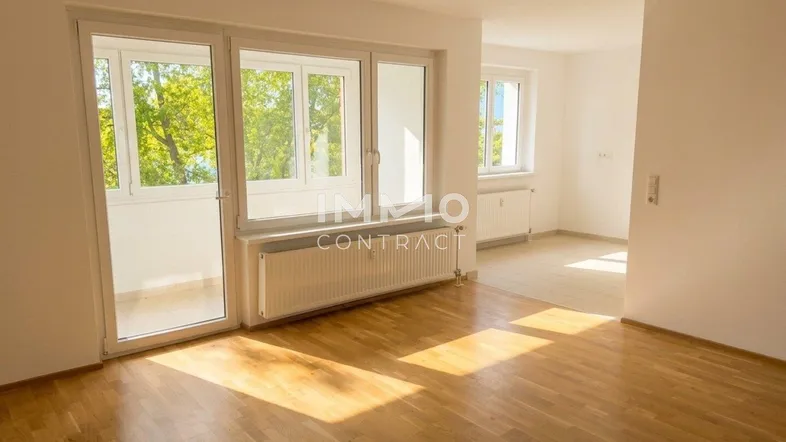 Helles Zimmer mit Parkettboden, großen Fenstern und Zugang zu einem Balkon, ideal als Wohnbereich.