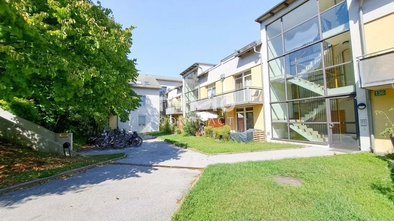 Mehrfamilienhaus-Komplex mit Grünflächen, Bäumen und Fahrradabstellplätzen im Freien.