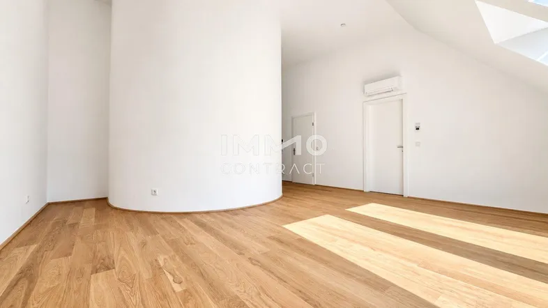 Heller Raum im Dachgeschoss mit Holzfußboden, weiß gestrichenen Wänden, Dachschrägen und viel natürlichem Licht.