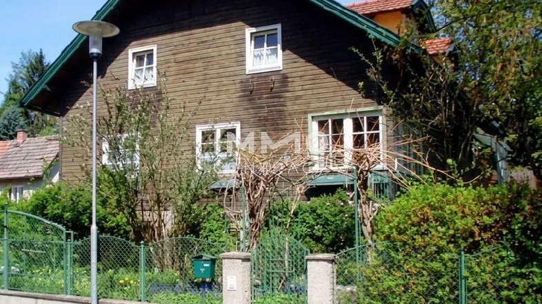 Traditionelles Holzhaus mit Satteldach, umgeben von einem grünen Garten und Zaun.