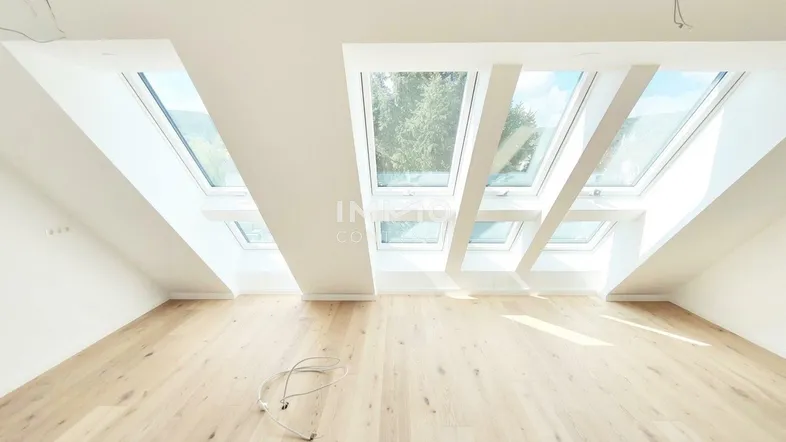 Heller Dachgeschossraum mit Holzboden, weißen Wänden und großen Dachfenstern.