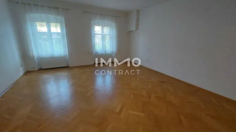 Geräumiges Zimmer mit Fischgrätparkett und zwei Fenstern, ideal als Wohn- oder Schlafzimmer.