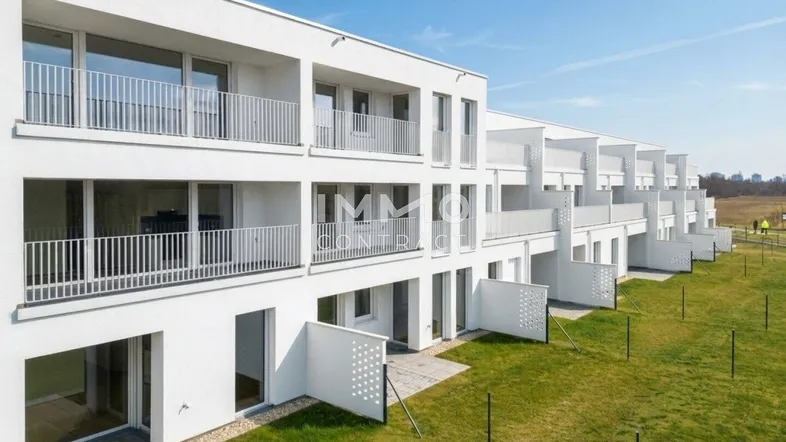 Moderne Wohnanlage mit weißen Fassaden, Balkonen und kleinen Gärten im Erdgeschoss.
