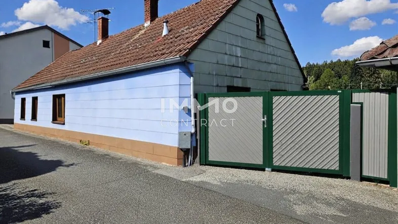 Ansicht eines Hauses mit hellblauer Fassade, braunem Ziegeldach und einem modernen grünen Einfahrtstor.