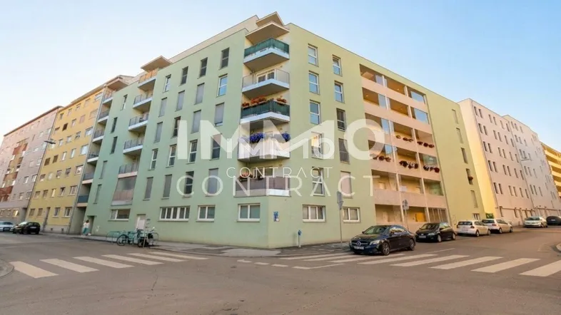 Mehrfamilienhaus an einer Straßenecke mit mehreren Balkonen und einer hellgrünen Fassade.