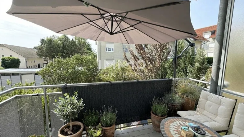 Möblierter Balkon mit Pflanzen und Sonnenschirm, bietet einen angenehmen Blick ins Grüne.