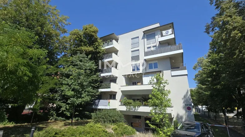Modernes Mehrfamilienhaus mit mehreren Balkonen, umgeben von Bäumen und Grünflächen.