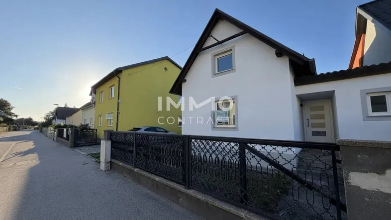Weißes Einfamilienhaus mit Satteldach und schmiedeeisernem Zaun an einer Wohnstraße.