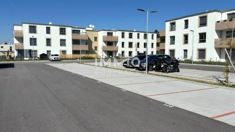 Moderne Wohngebäude mit weißer Fassade und großem Außenparkplatz unter blauem Himmel.