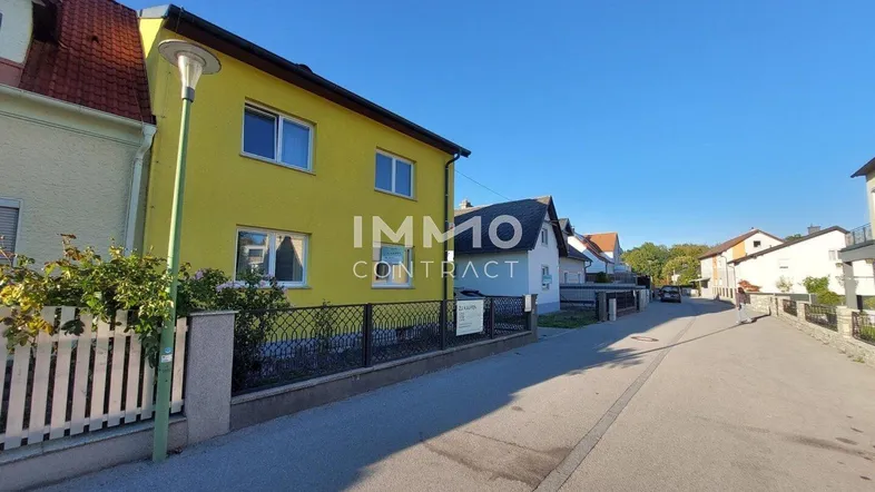 Gelbes Wohnhaus mit rotem Ziegeldach und Vorgarten an einer ruhigen Straße gelegen.