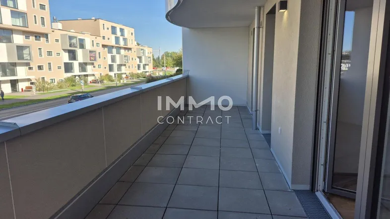 Geräumiger Balkon mit Fliesenboden und Blick auf die umliegenden modernen Gebäude und die Straße.