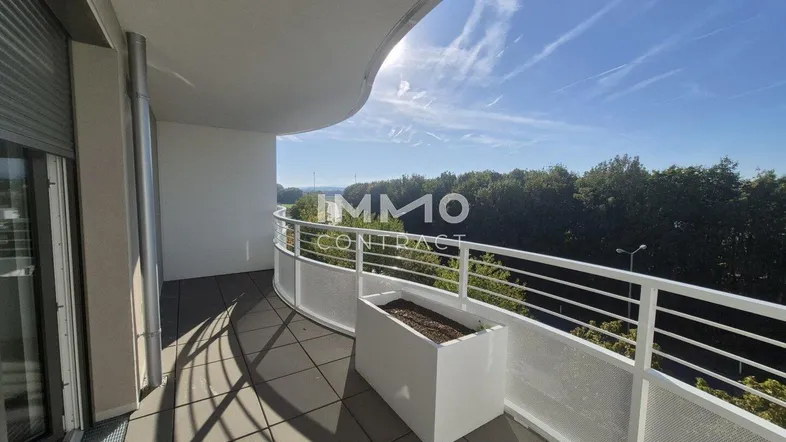 Geräumiger Balkon mit geschwungener Brüstung und weitem Blick ins Grüne unter blauem Himmel.