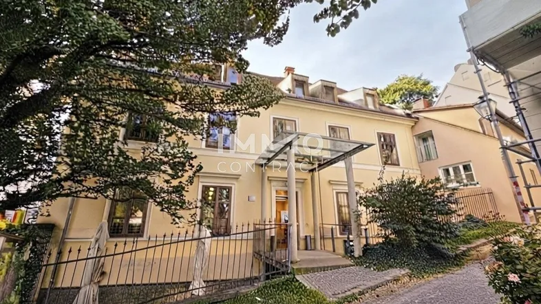 Historisches Gebäude mit gelber Fassade, umgeben von Bäumen und einer gepflasterten Zufahrt.