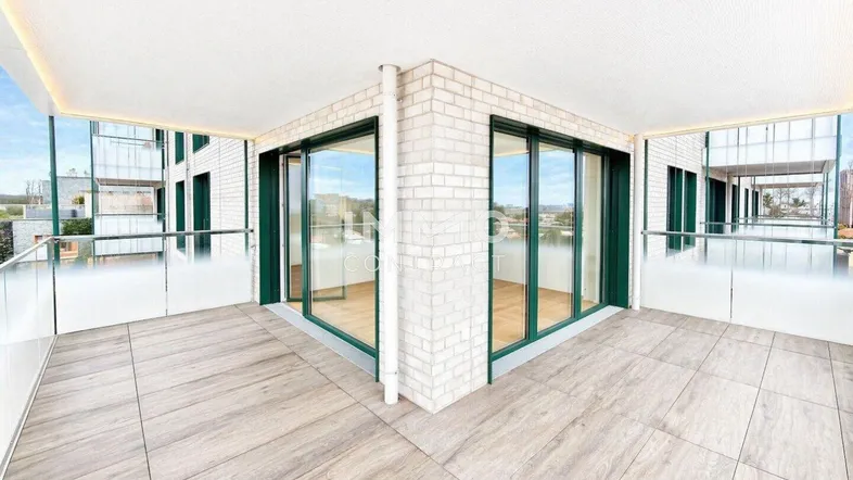 Großer Eckbalkon mit Fliesenboden und Glasgeländer, bietet weite Aussicht über die Umgebung.