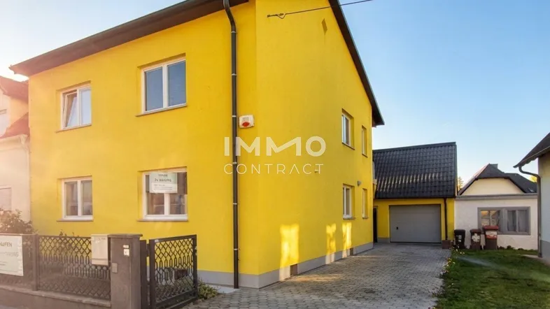 Gelbes Einfamilienhaus mit gepflasterter Einfahrt und Garage unter blauem Himmel.