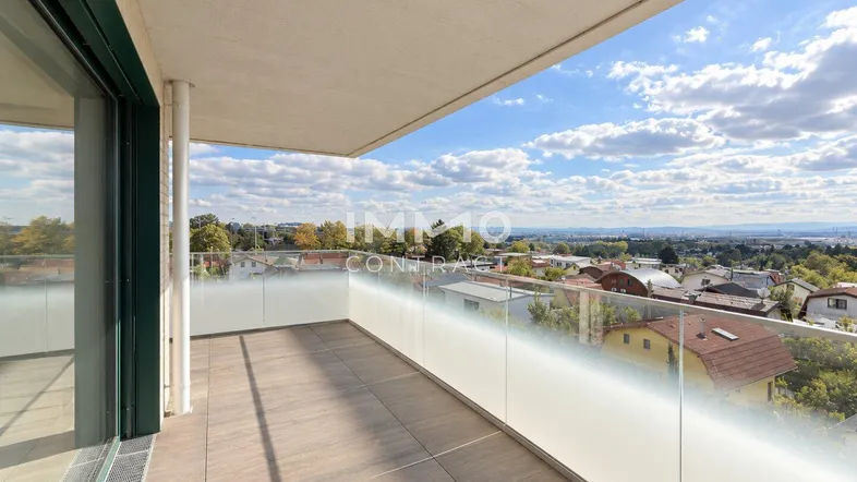 Geräumiger Balkon mit Glasbrüstung und weitem Blick über die Stadt und die umliegende Landschaft.