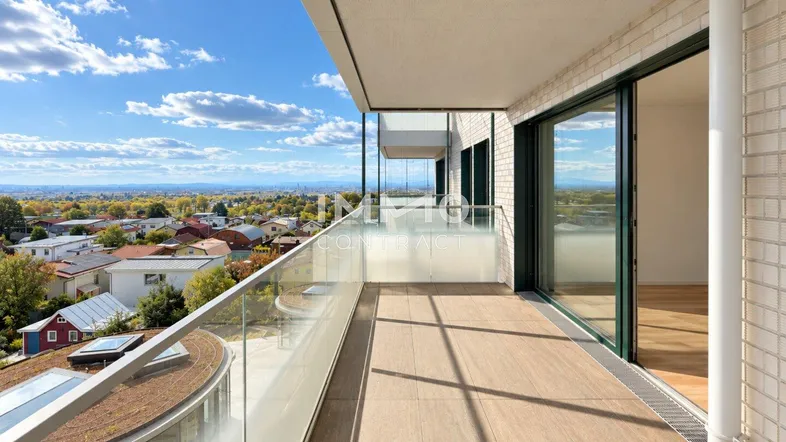 Geräumiger Balkon mit Glasgeländer und weitem Blick über die Stadt und die grüne Umgebung.
