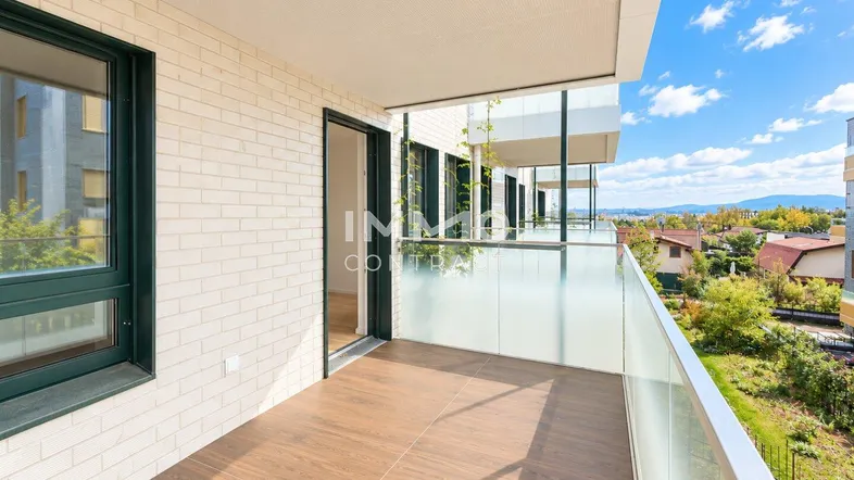Heller Balkon mit Glasgeländer, Holzboden und weitem Blick über die Umgebung.