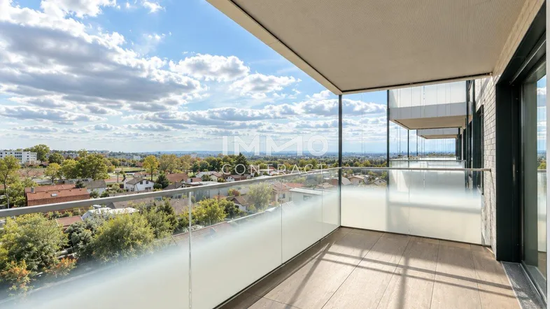 Geräumiger Balkon mit Glasgeländer, Fliesenboden und weitem Blick über die Stadt und grüne Umgebung.