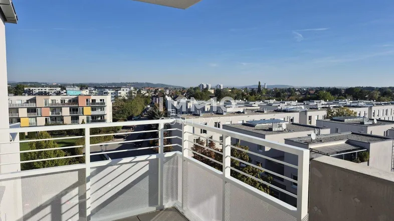 Heller Balkon mit Weitblick über die Stadt und umliegende Wohngebäude unter blauem Himmel.