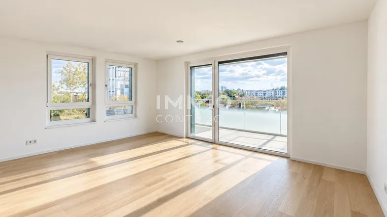Helles Zimmer mit Holzboden, großen Fenstern und Zugang zu einem Balkon mit Wasserblick.