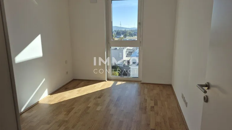 Helles Zimmer mit Parkettboden und großem Fenster, bietet viel Tageslicht und Ausblick.