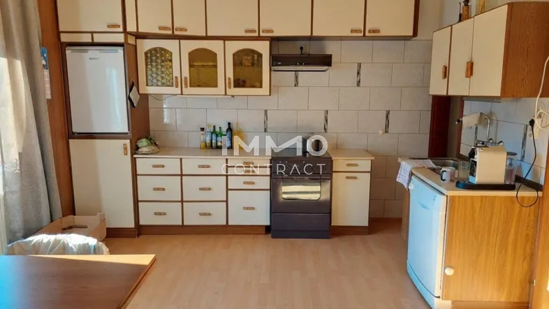 Ältere Küche mit hellen Schränken, Fliesenrückwand, Holzbalkendecke und Laminatboden.