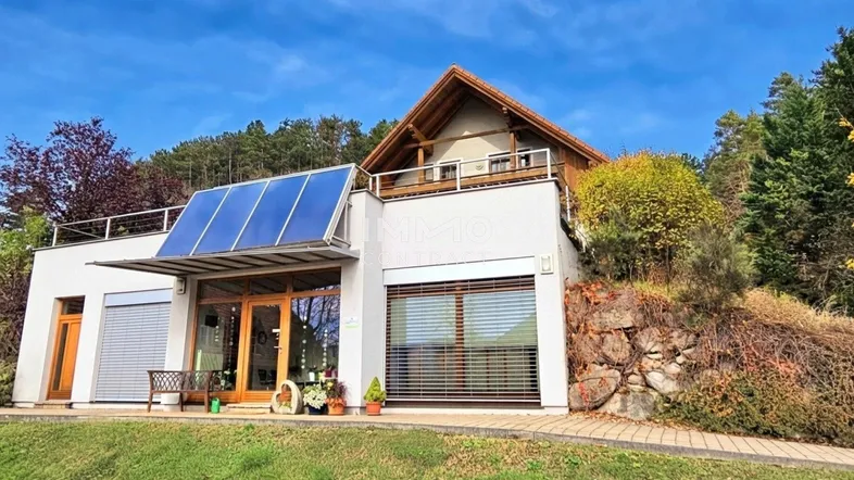 Modernes Haus mit Solarpaneelen auf dem Dach und Balkon in ländlicher Umgebung.