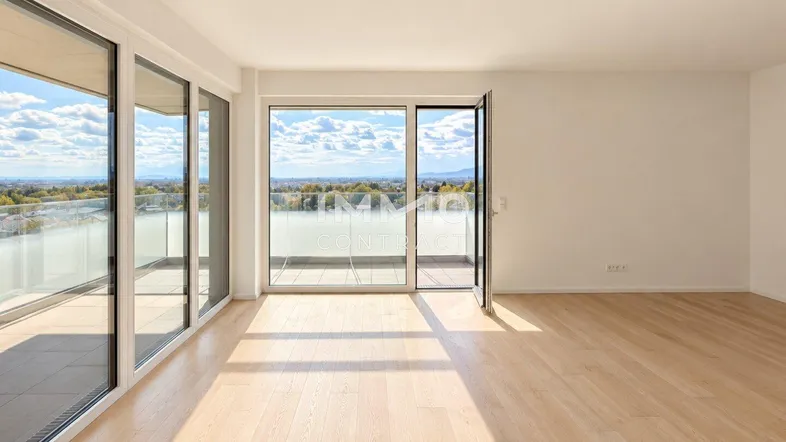 Helles, leeres Wohnzimmer mit Holzboden und großen Fenstern, die Zugang zu einem Balkon bieten.