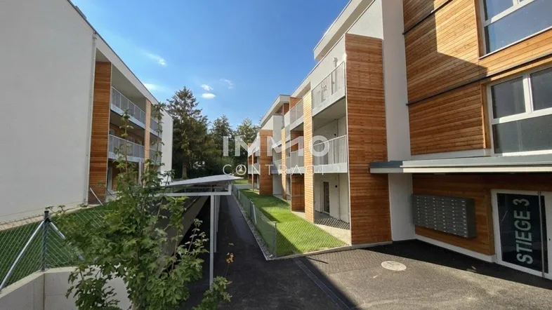Moderne Wohngebäude mit Holzfassaden, Balkonen und begrünten Außenbereichen unter blauem Himmel.