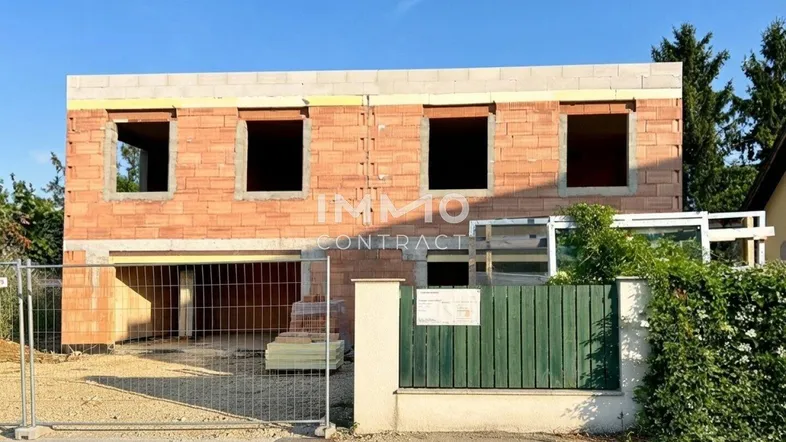 Rohbau eines modernen Doppelhauses mit großen Fensteröffnungen und massiver Bauweise.