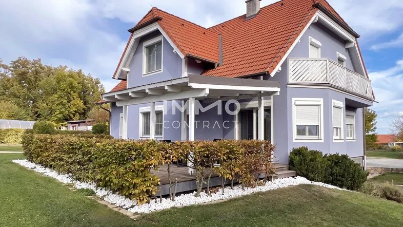 Modernes Einfamilienhaus mit lila Fassade, rotem Ziegeldach und gepflegtem Vorgarten.