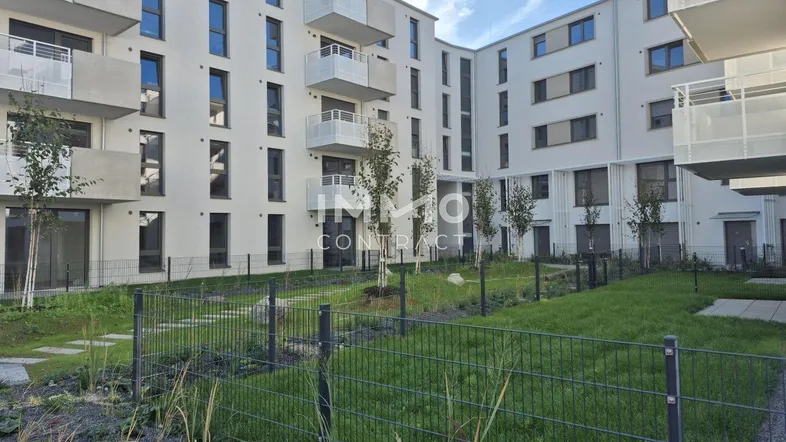 Modernes Mehrfamilienhaus mit weißer Fassade und kleinen Balkonen, umgeben von einer Grünfläche.