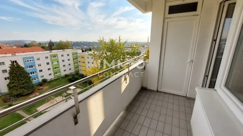Balkon mit Fliesenboden und Blick auf die umliegenden Gebäude und grüne Landschaft.