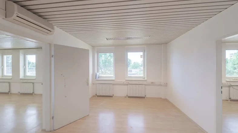 Helles, leeres Büro mit Holzfußboden, weißen Wänden und Klimaanlage, bereit zur individuellen Gestaltung.