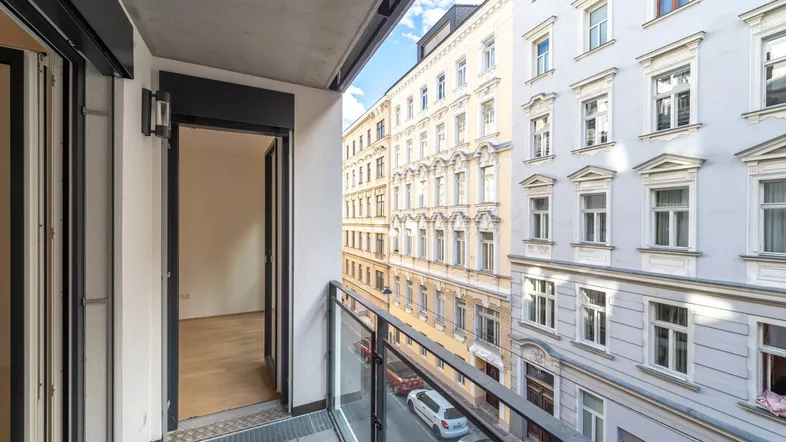 Schmaler Balkon mit Glasbrüstung und Blick auf die gegenüberliegenden Gebäude der Stadt.