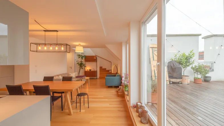 Heller offener Wohn- und Essbereich mit Holzboden und Zugang zu einer großen Dachterrasse.