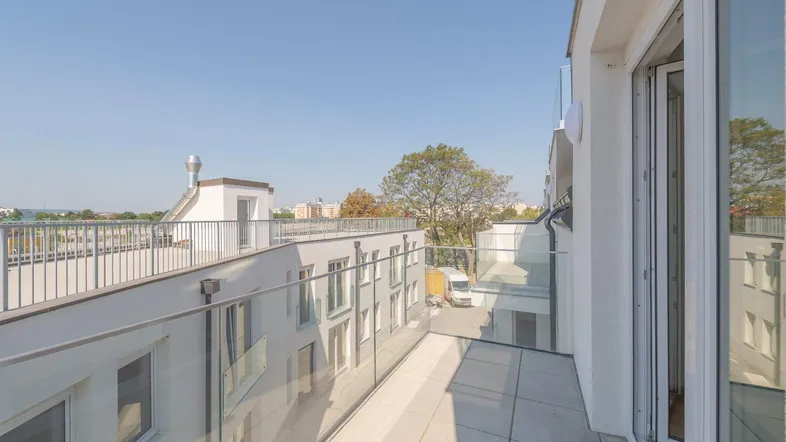 Heller Balkon mit Glasgeländer und Blick auf die umliegenden Gebäude unter blauem Himmel.