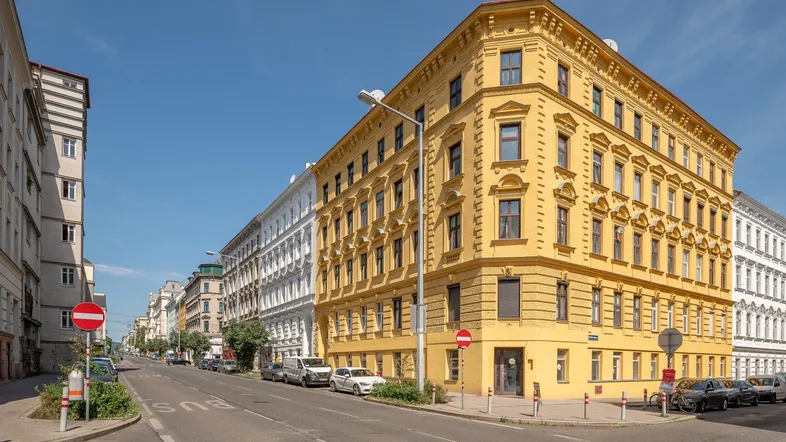 Historisches Eckgebäude in Gelb an einer belebten Stadtstraße unter blauem Himmel.